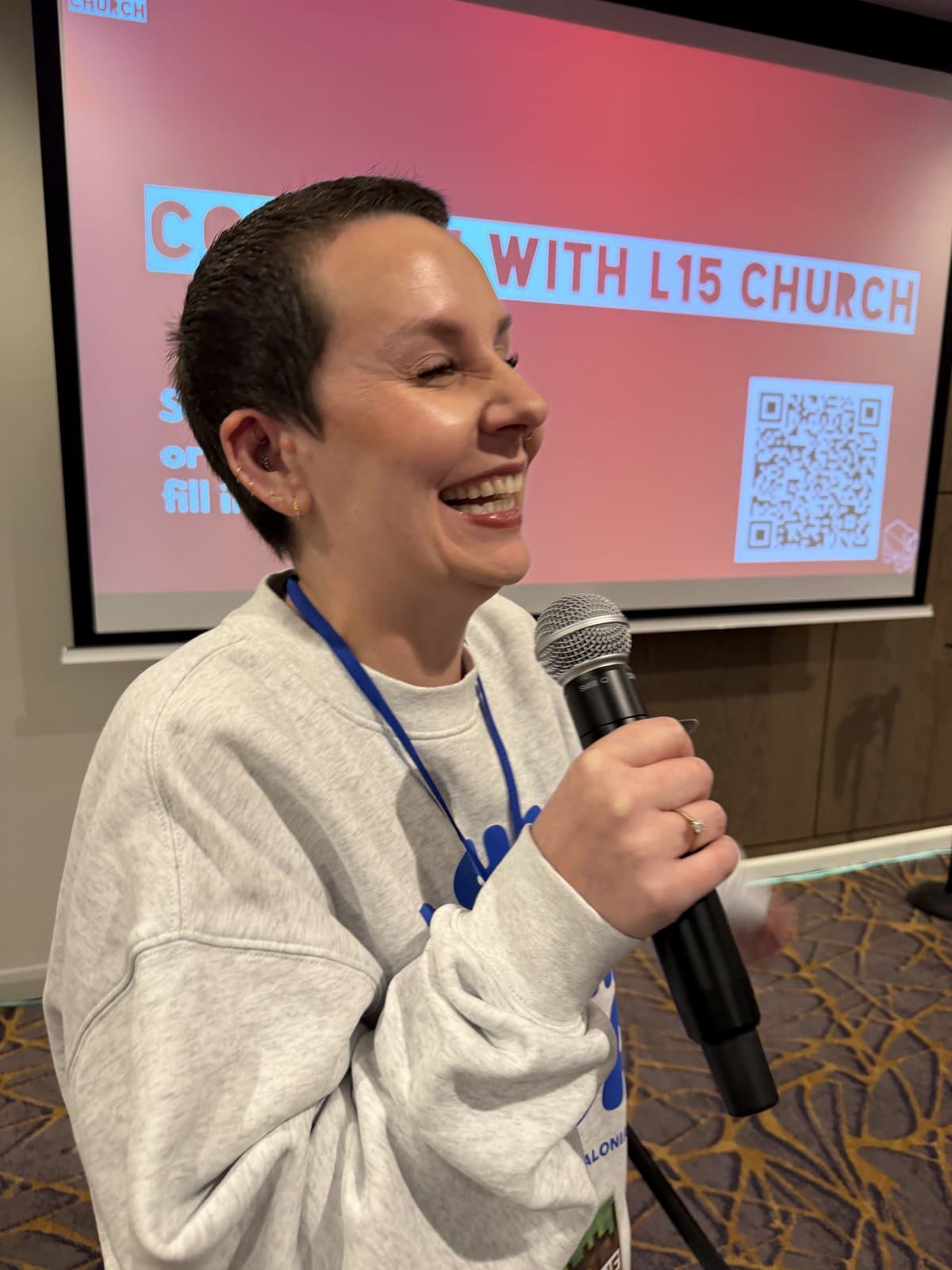 A smiling L15 team member with a microphone welcomes people at a Sunday service